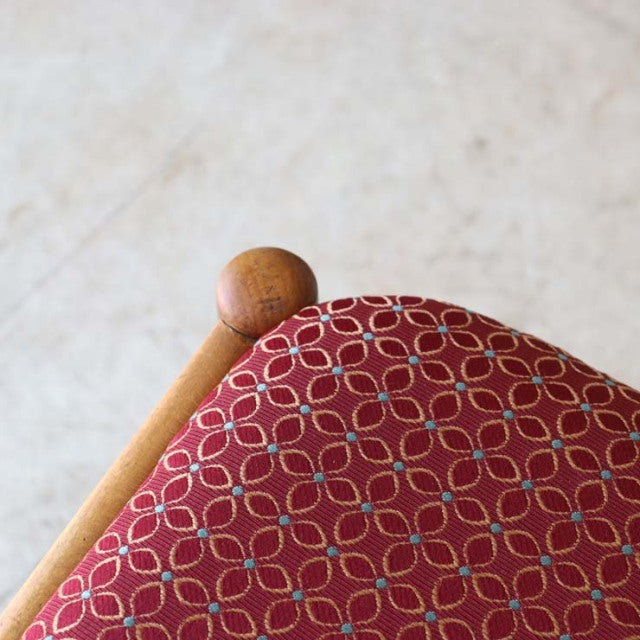 Close-up of vintage teak dining chair seat with red fabric featuring a mid-century British geometric flower pattern, smooth.