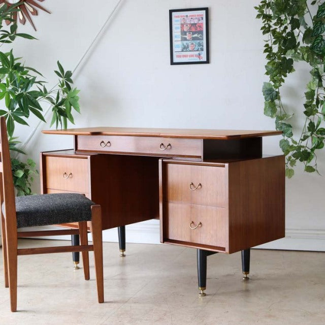 Vintage British mid-century teak desk by G-PLAN with sleek wood grain, brass-capped tapered legs, and three drawer units.