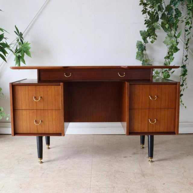 Vintage mid-century teak G-PLAN desk with rich wood grain, two drawer stacks, brass ring pulls, and tapered black legs with.