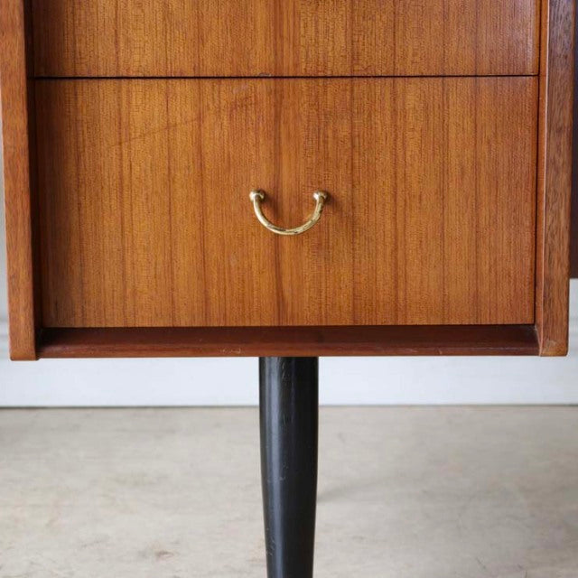 Mid-century British G-PLAN teak desk corner with rich wood grain, brass handle, and tapered black leg.