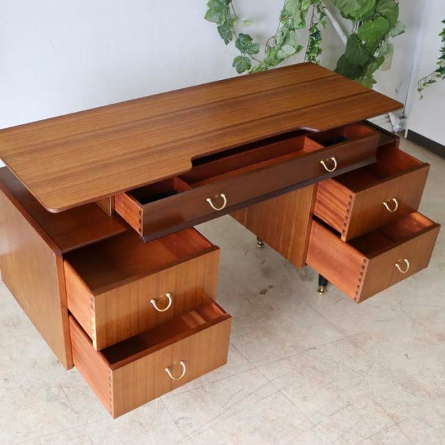 Vintage British G-Plan teak desk with mid-century design, rich wood grain, brass handles, and tapered legs.