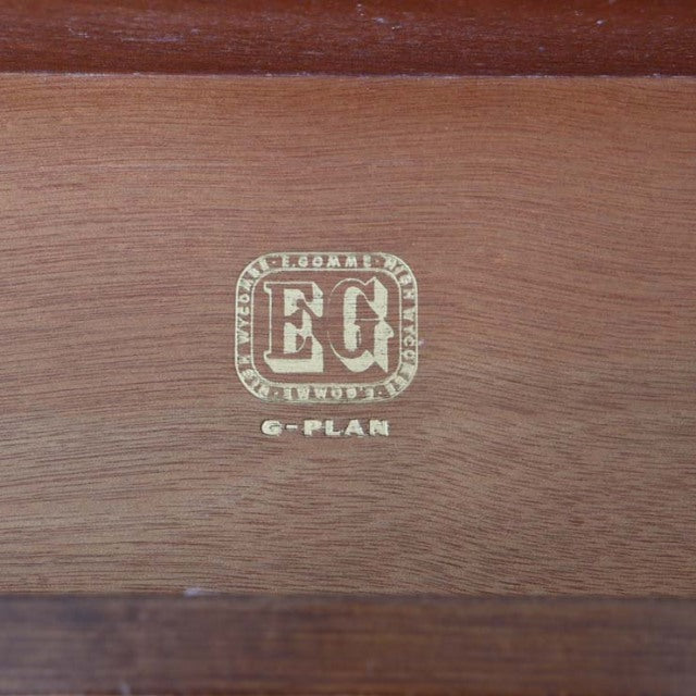 Close-up of vintage G-PLAN British mid-century teak wood logo stamped on smooth grain surface.