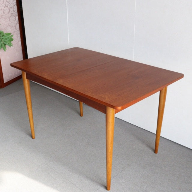 Mid-century British vintage teak dining table with smooth wood grain and slender tapered legs from Denmark style.