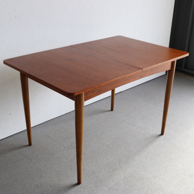 Mid-century British teak dining table with smooth wood grain, tapered round legs, and rectangular top.