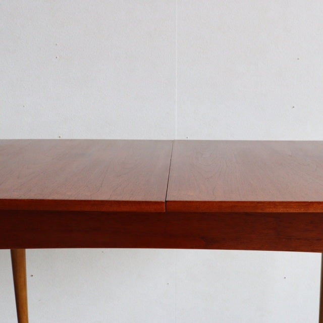 Mid-century British vintage teak dining table with rich wood grain and clean rectangular form, supported by slender tapered.