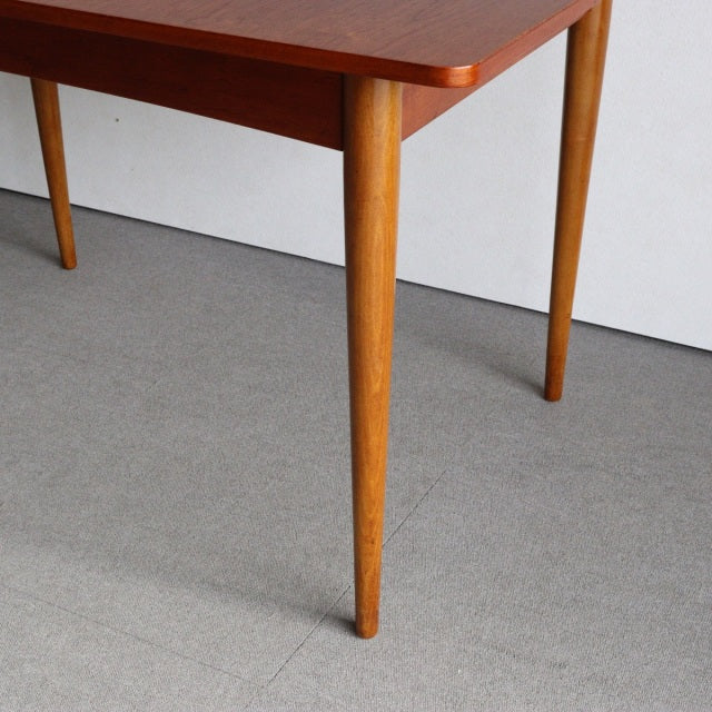 Mid-century vintage teak dining table with tapered round legs and smooth wood grain, British-Denmark style.