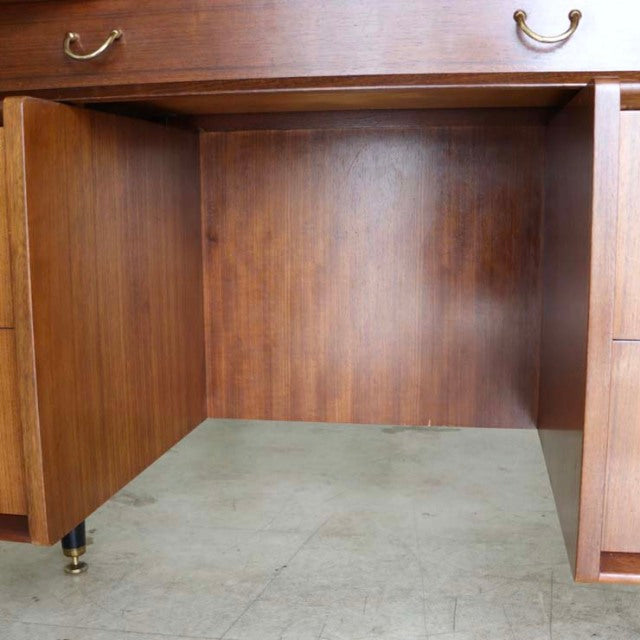 Mid-century British G-PLAN teak desk with rich wood grain, brass handles, and tapered legs on brass caps.