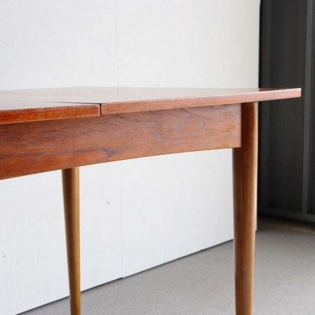 Mid-century British teak dining table with smooth wood grain, rounded tapered legs, and rectangular top showcasing vintage.