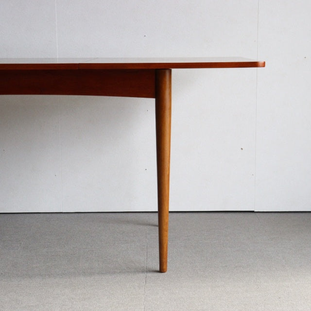 Mid-century vintage British teak dining table with smooth wood grain and tapered round legs.
