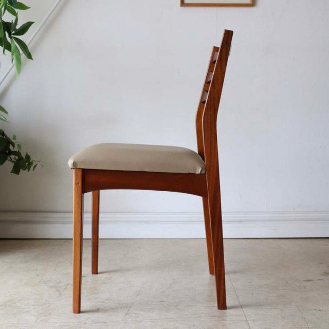 Mid-century British vintage teak dining chair with beige upholstered seat and tapered legs, side view.