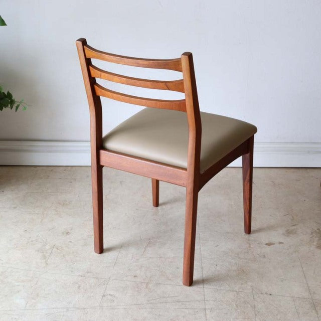 Mid-century vintage teak dining chair from Britain with a beige upholstered seat, horizontal slat backrest, and tapered legs.