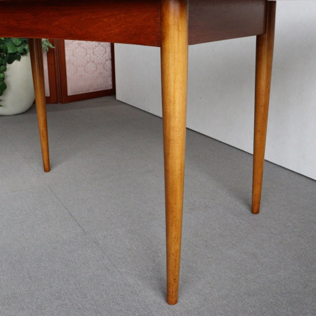 Mid-century British teak dining table with smooth wood grain and tapered round legs in light brown finish.