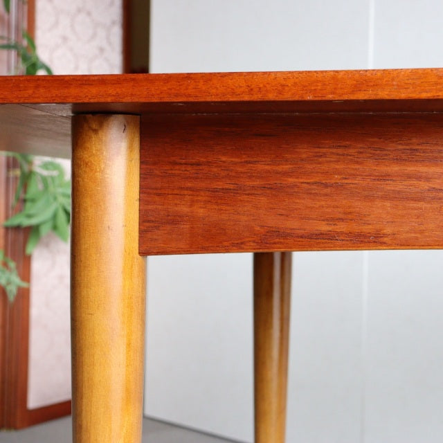 Mid-century British vintage teak dining table corner with rich wood grain and tapered round legs.
