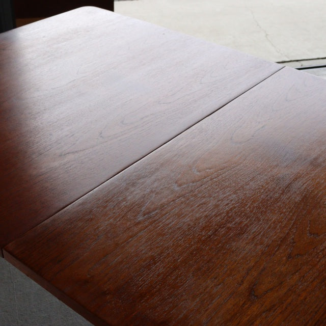 Mid-century British teak dining table with rich wood grain and smooth rectangular top, Denmark style legs visible.