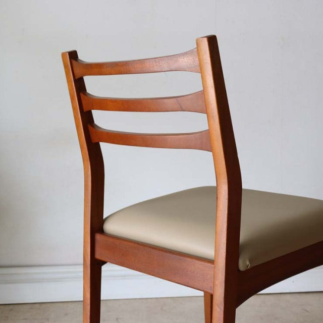 Mid-century British vintage teak dining chair with ladder back and beige upholstered seat, smooth wood grain visible.