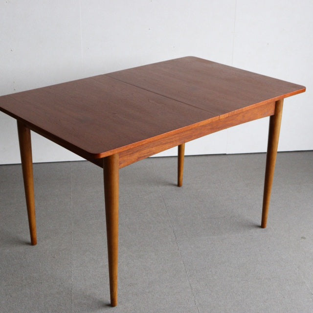 Mid-century vintage British teak dining table with rectangular top and slender tapered legs showcasing rich wood grain.