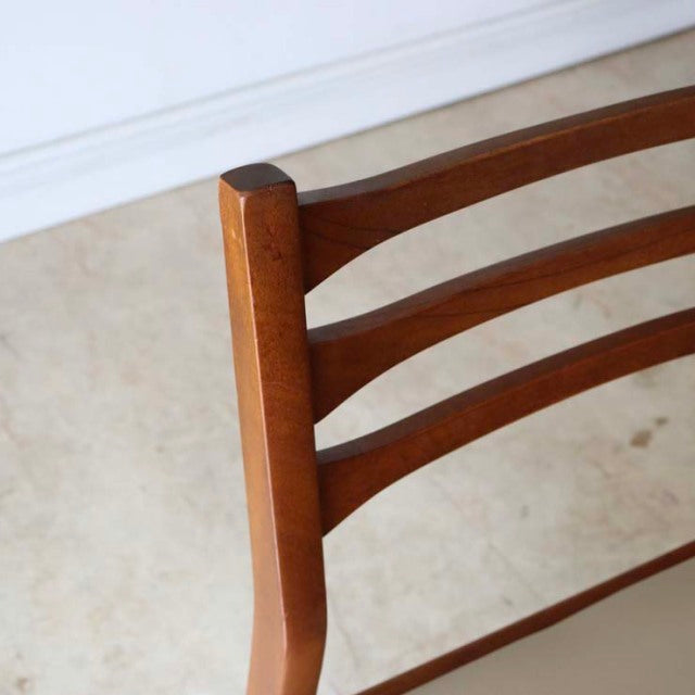 Close-up of vintage teak mid-century British dining chair backrest with smooth wood grain and curved horizontal slats.