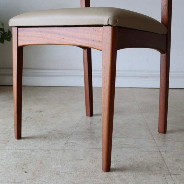 Set of four vintage British mid-century teak dining chairs with cream upholstered seats and tapered legs, showcasing sleek.
