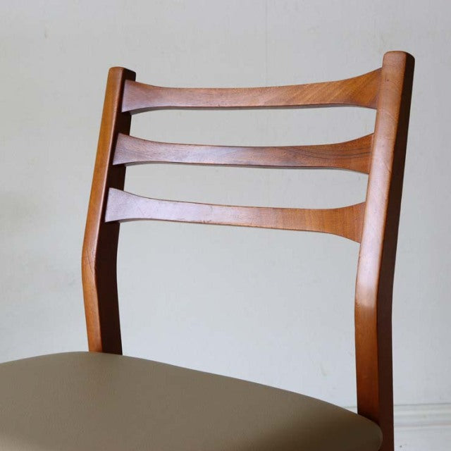 Mid-century vintage British teak dining chair with curved ladder back and smooth wood grain, light beige upholstered seat.
