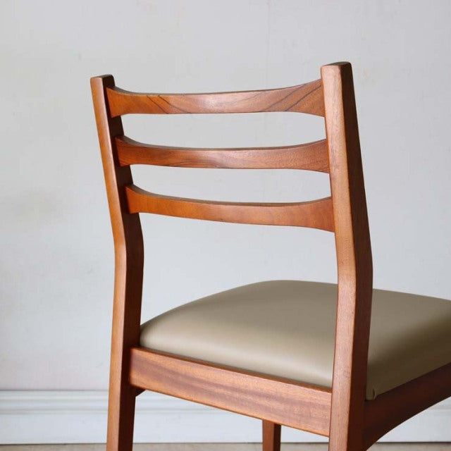 Set of four vintage mid-century British dining chairs with teak frames and beige upholstered seats, featuring sleek, curved.