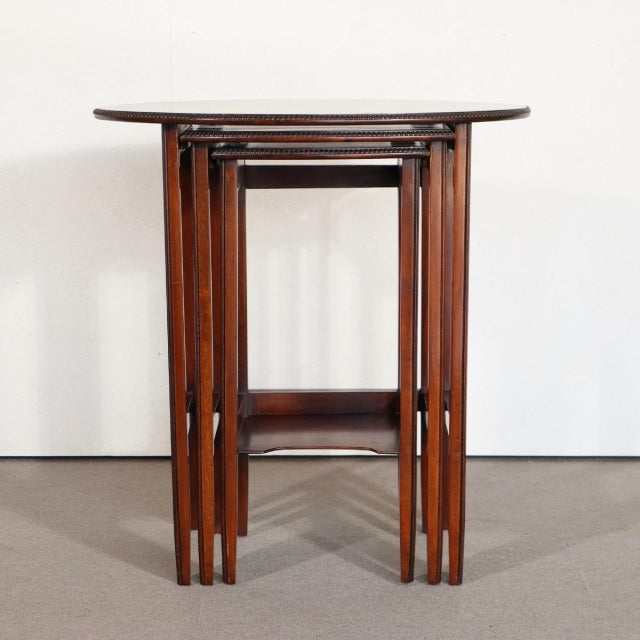 Set of three vintage British teak nest tables with rich wood grain, slender tapered legs, and mid-century Denmark design.