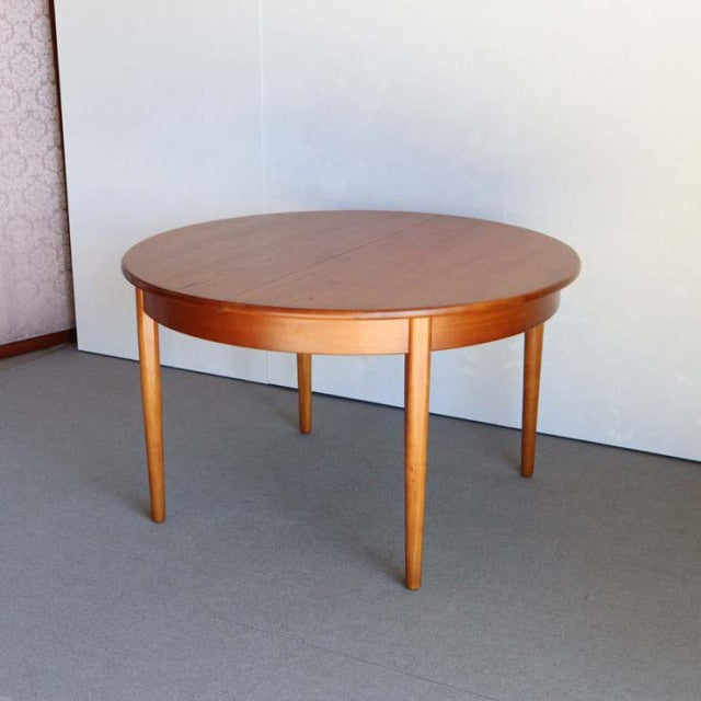Round vintage teak dining table with smooth grain, slender tapered legs, British mid-century Danish design.