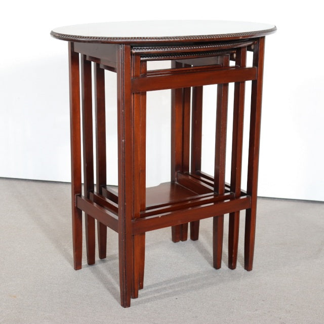 Set of three British mid-century teak nest tables with rich wood grain, slender legs, and geometric frame design.