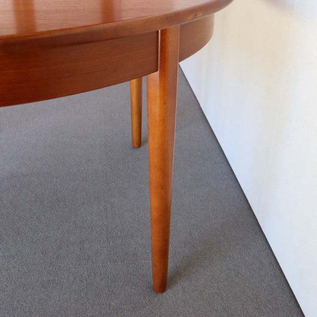 Round mid-century British vintage dining table in teak with smooth grain and tapered legs.