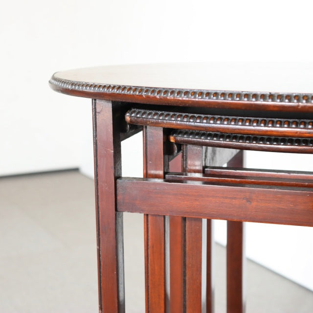 Set of three vintage British teak mid-century nest tables with rich wood grain, rounded edges, and slender tapered legs.