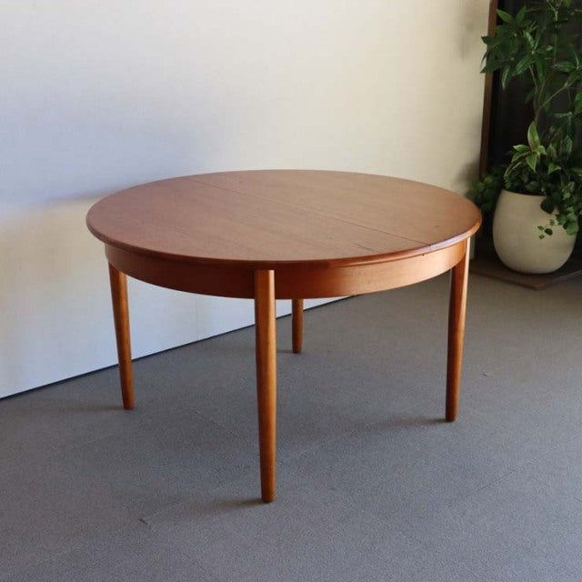 Round mid-century vintage teak dining table with smooth wood grain and tapered legs, British-Denmark style.