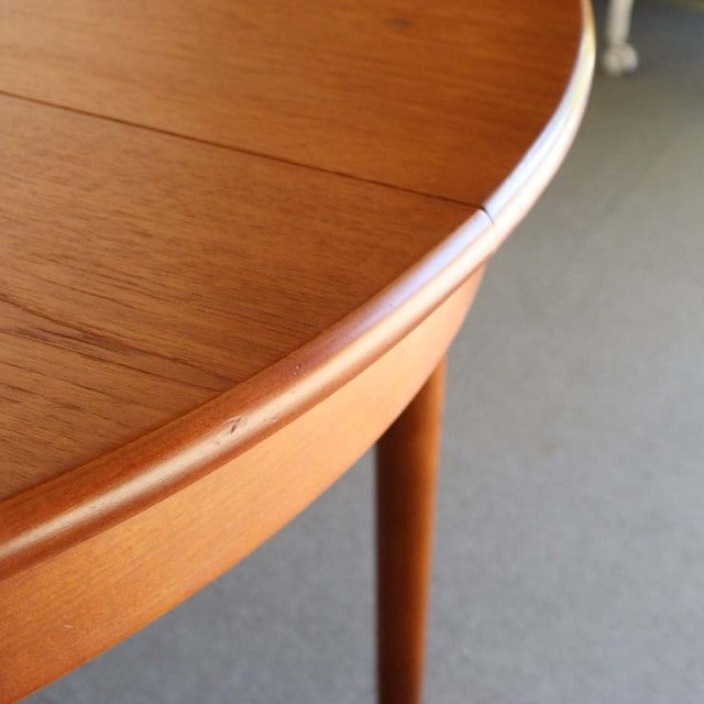 Round vintage teak dining table with smooth wood grain, tapered mid-century British legs, Danish design influence.