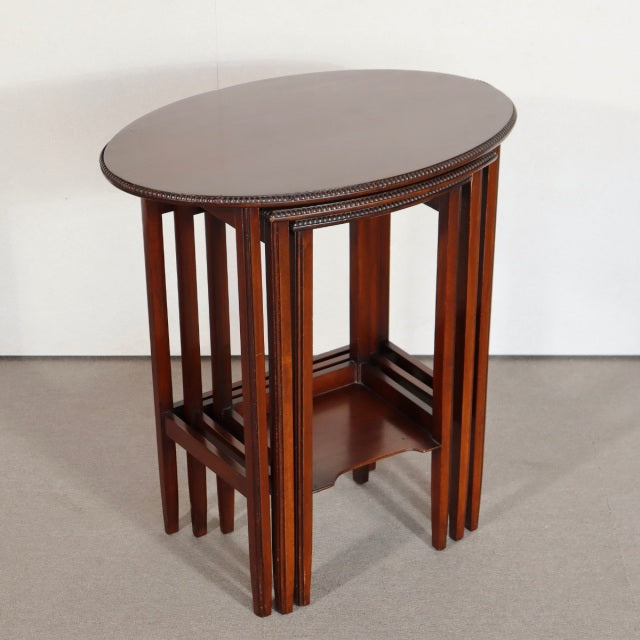 Vintage British mid-century teak nest tables with rich wood grain, slender vertical legs, and smooth oval tops.
