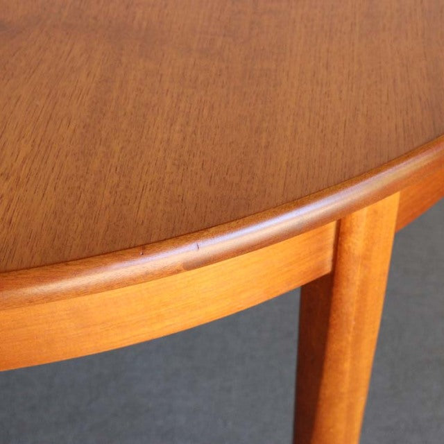 Vintage mid-century British teak round dining table with smooth wood grain and tapered legs.