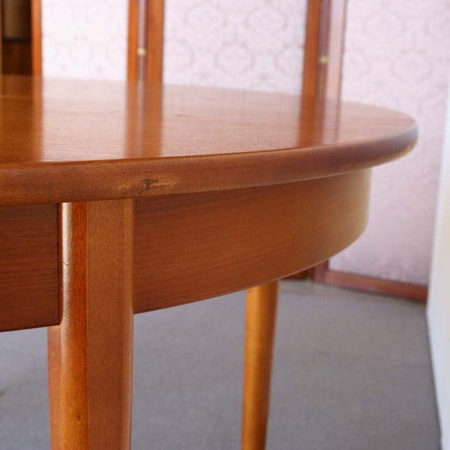 Mid-century British vintage teak round dining table with smooth wood grain and slender tapered legs.