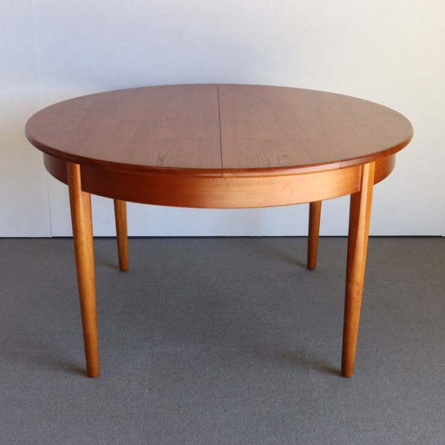 Round mid-century teak dining table with smooth wood grain, tapered British vintage legs, Danish design.