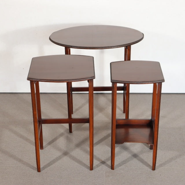 Set of three British vintage mid-century teak nest tables with tapered legs and rich wood grain.