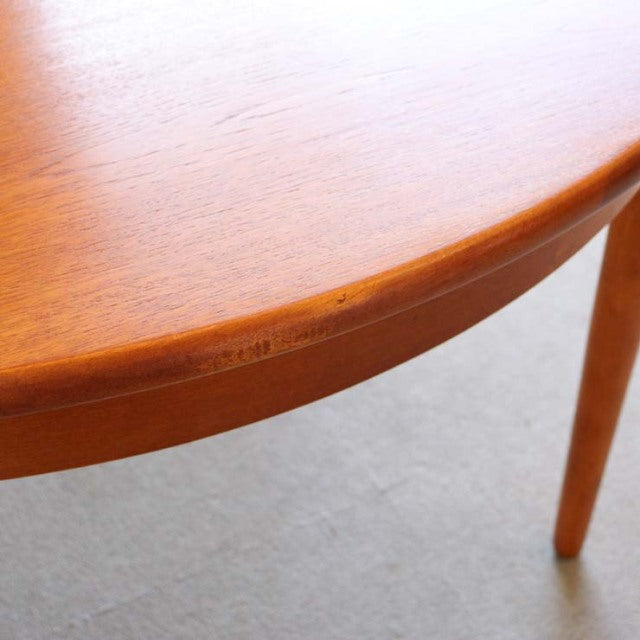 Vintage British mid-century teak round dining table with smooth wood grain and tapered legs.