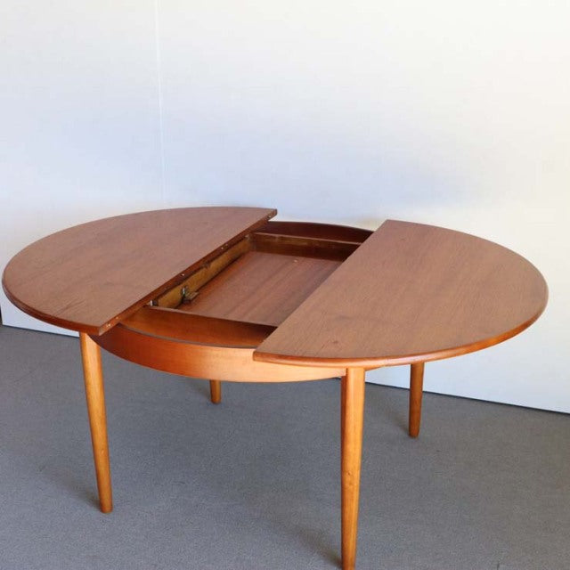 Vintage British mid-century teak round dining table with tapered legs and a split top extension mechanism.