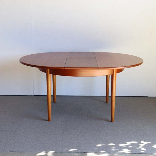 Mid-century vintage British teak dining table with round top, smooth wood grain, and slender tapered legs from Denmark.