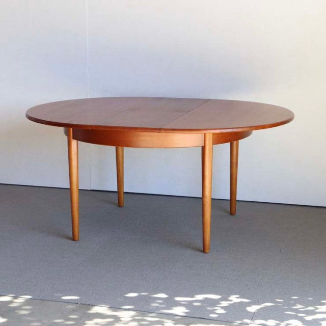 Vintage British mid-century round teak dining table with smooth wood grain and tapered legs, Denmark style.