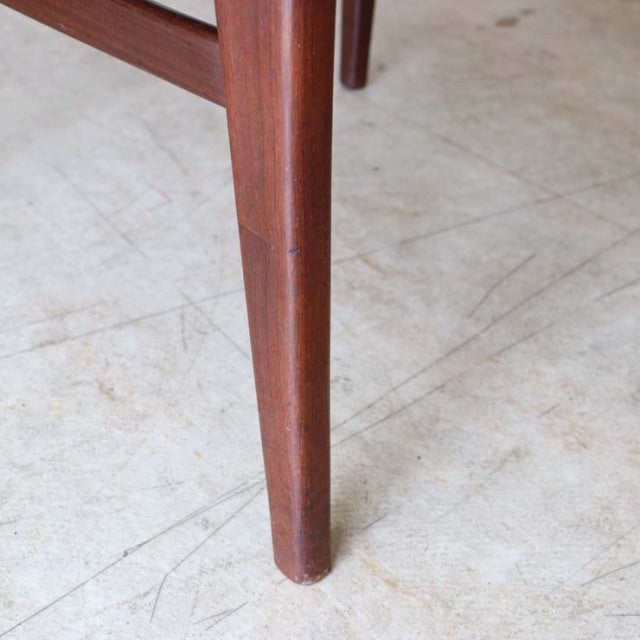 Mid-century British vintage teak dining chair leg with smooth wood grain and tapered design on light floor.