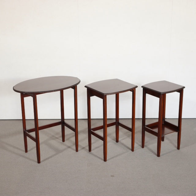 Set of three vintage British teak mid-century nest tables with oval and square tops, slender tapered legs, and crossbar.