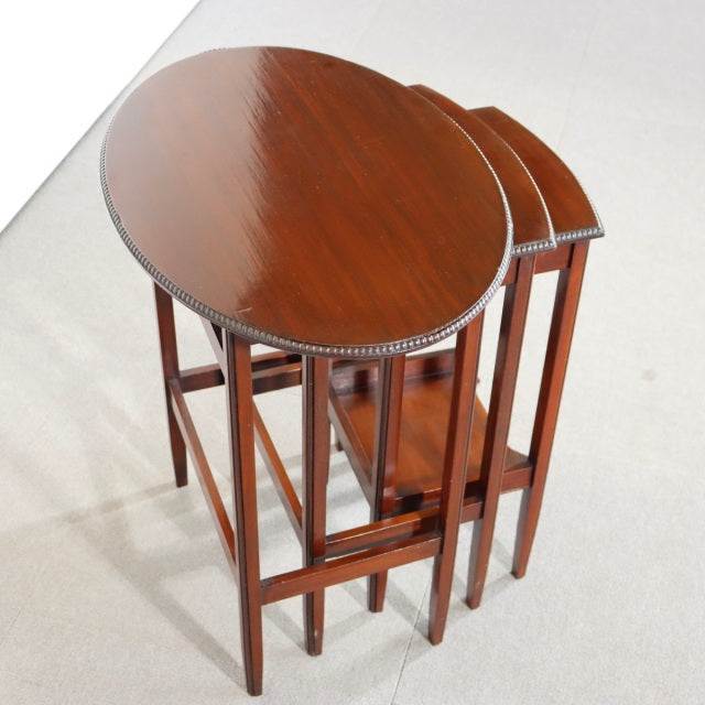 Set of British mid-century vintage teak nest tables with oval tops, fine wood grain, and slender square legs.
