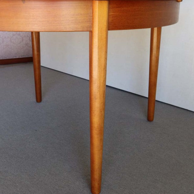 Mid-century vintage teak round dining table with smooth grain and slender tapered legs, British-Danish design.