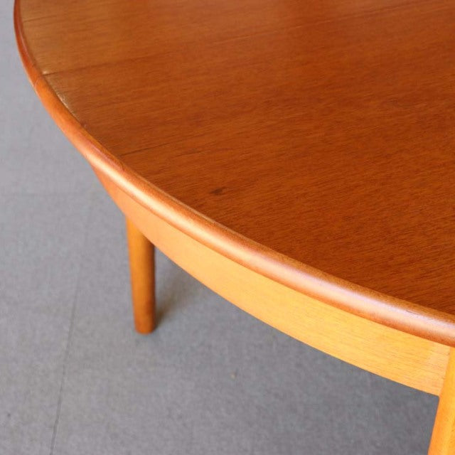 Round vintage teak dining table with smooth wood grain, British mid-century design, slender legs, Denmark style influence.