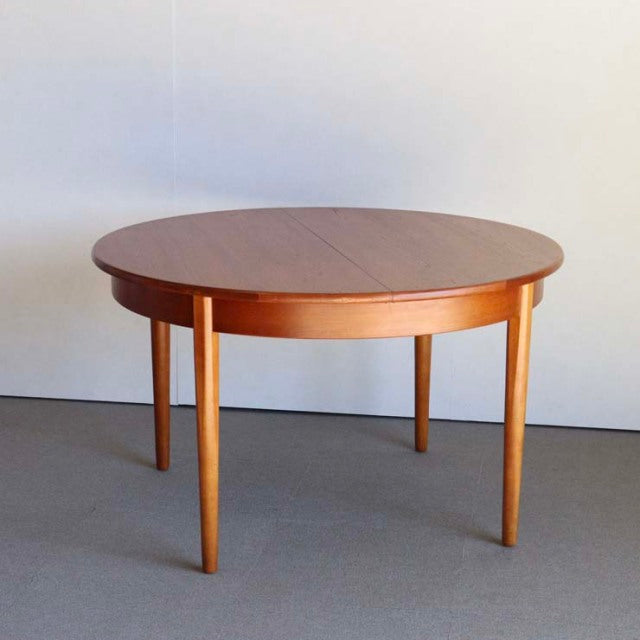 Round vintage teak dining table with smooth grain, tapered legs, mid-century British and Danish design.