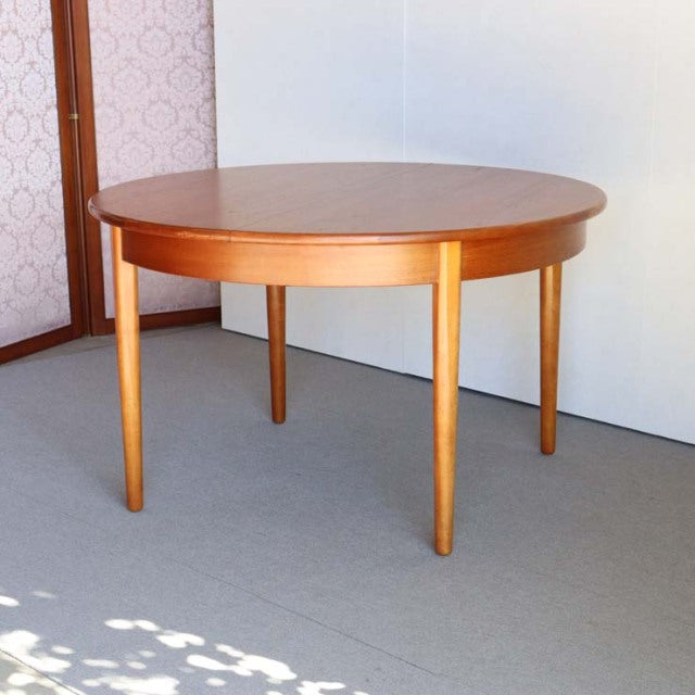 Round vintage teak dining table with smooth grain, British mid-century design, four tapered legs, Danish influence.