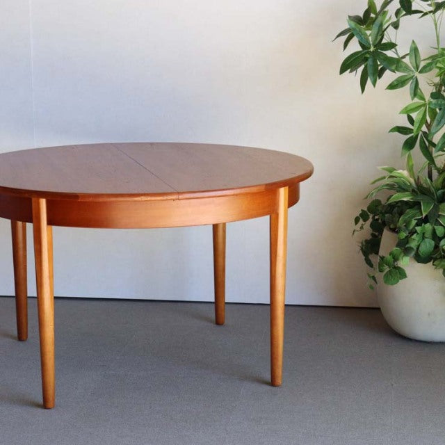 Vintage mid-century British teak round dining table with smooth wood grain and tapered legs.