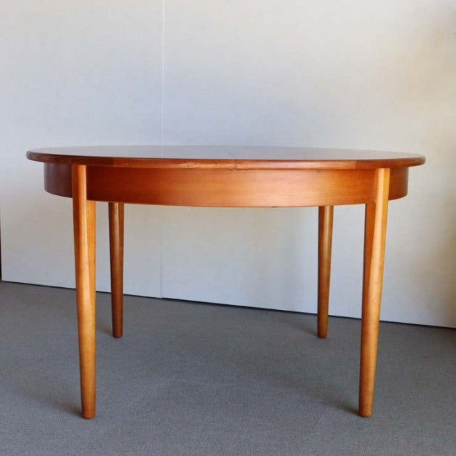 Vintage mid-century teak dining table with smooth round top, tapered legs, and British-Denmark design influences.