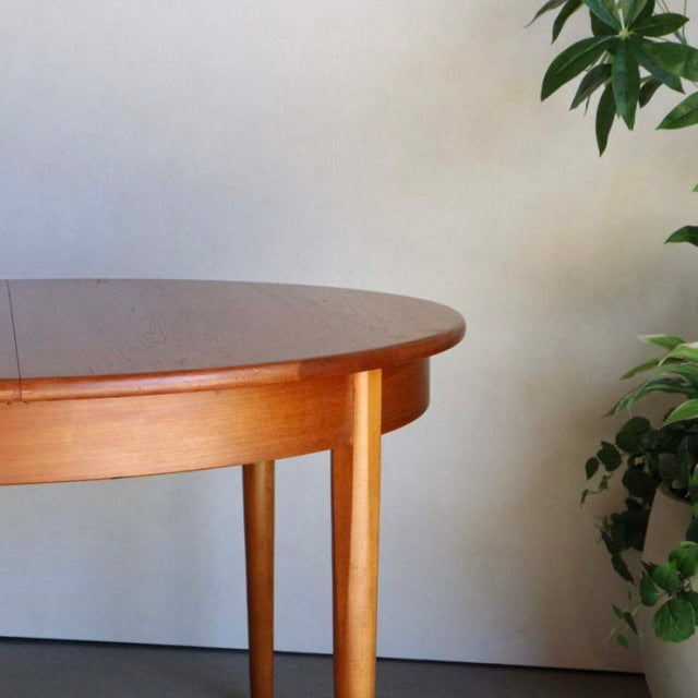 Mid-century British vintage teak round dining table with smooth wood grain and slender tapered legs.